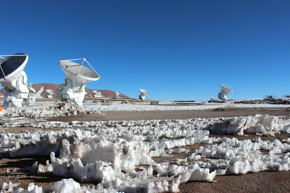 White ALMA radio telescope dishes across a snow-covered high-altitude plateau under a clear blue sky