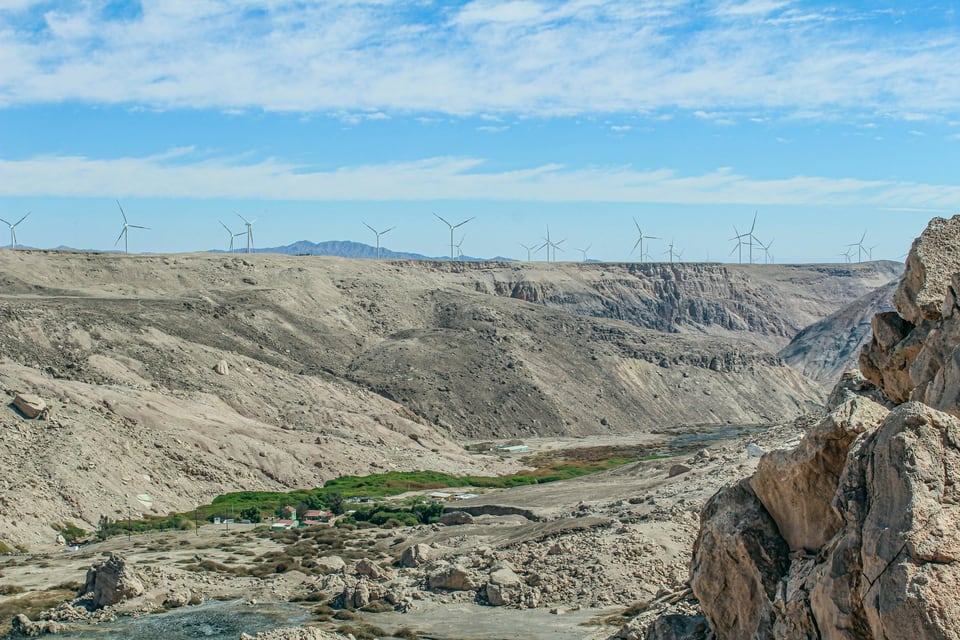 Line of wind turbines above a pale desert ravine near Calama under a blue, cloud-streaked sky