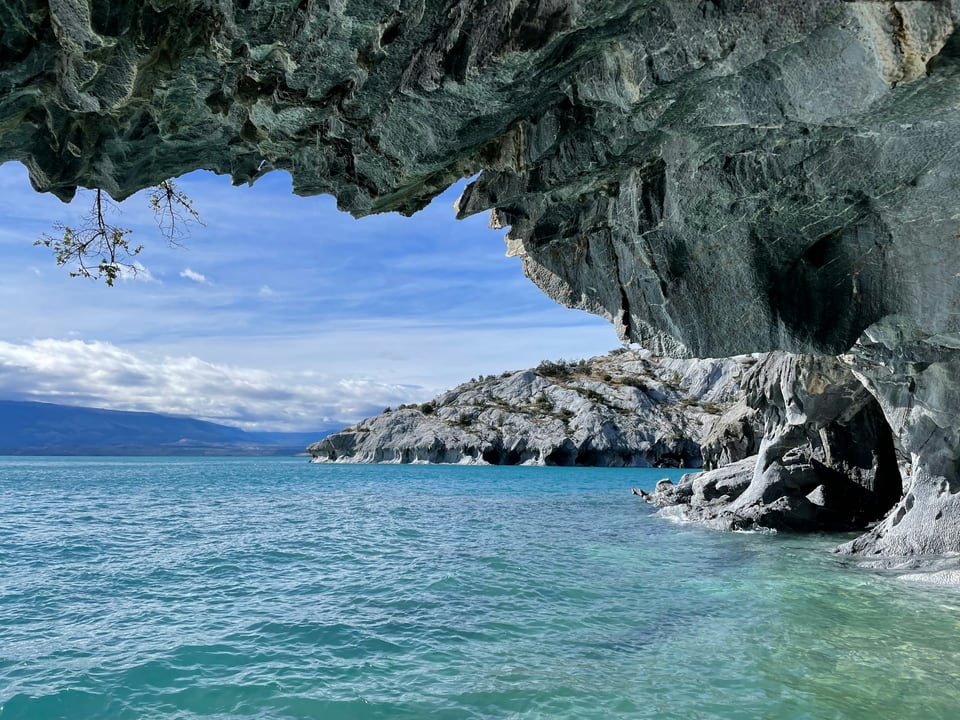 Turquoise water and a distant mountain framed by the carved grey rock of the Marble Caves