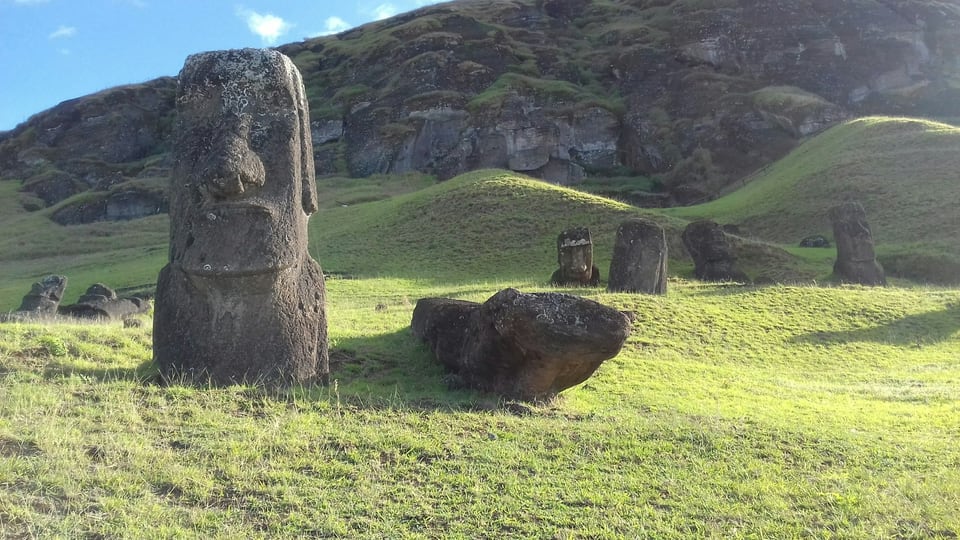 Standing and partially buried moai among green slopes and exposed volcanic rock at Rapa Nui