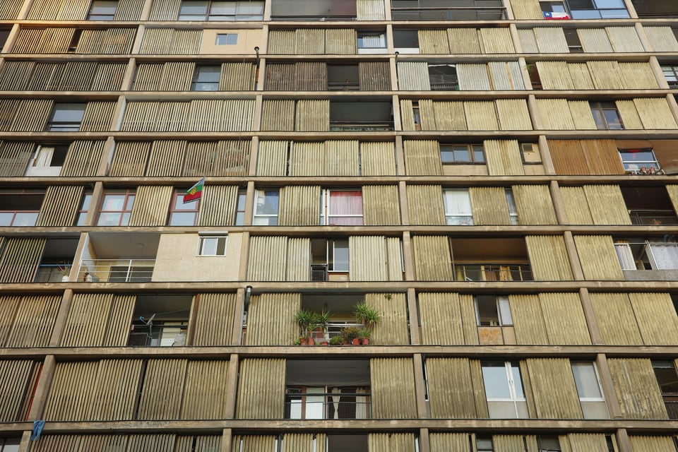 Grid of concrete balconies and vertical timber screens across a residential building façade in Santiago