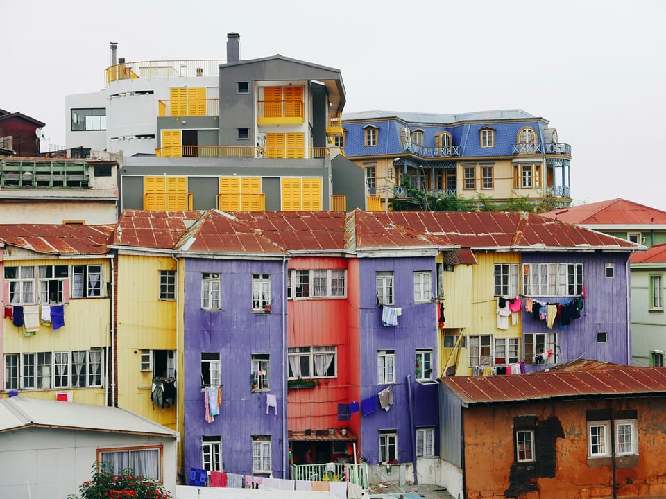 Rows of yellow, purple, red and blue hillside building façades with corrugated roofs in Valparaíso
